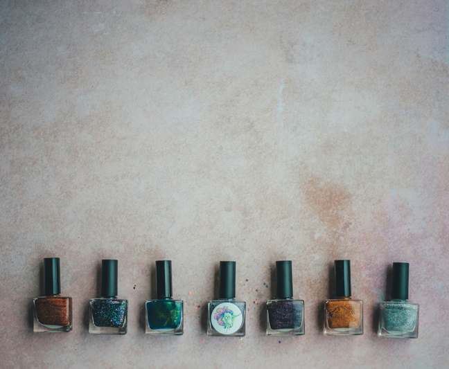 Close-up of colorful nail art tools including dotting pens, brushes, and rhinestone trays on a pastel pink surface
